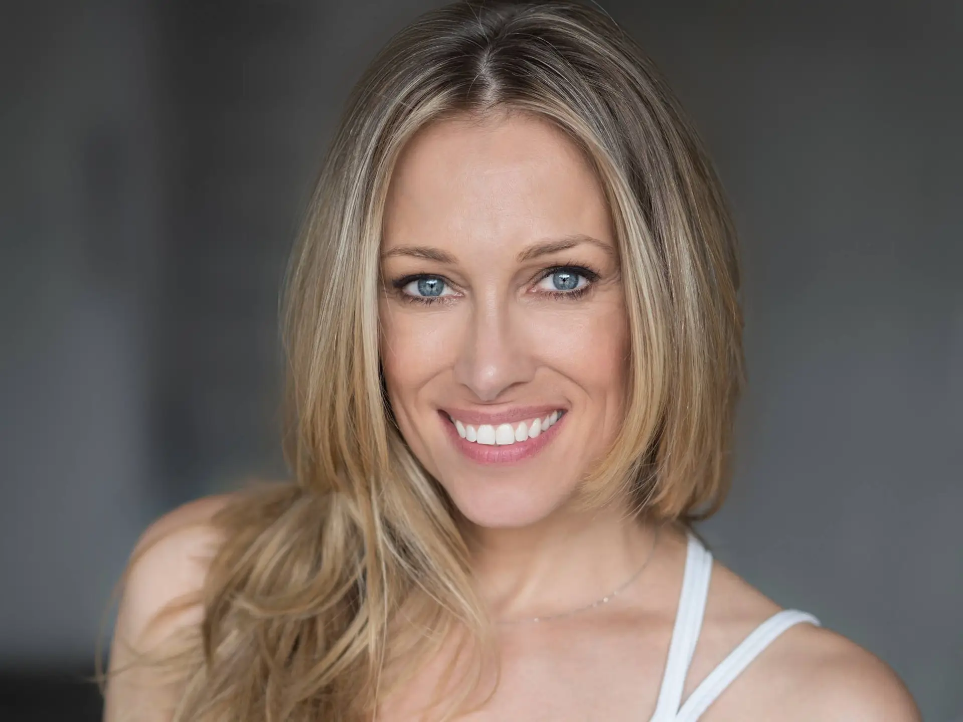 Close Up Portrait of a Smiling Woman with Blue Eyes and Long Blonde Hair Wearing a Light Top