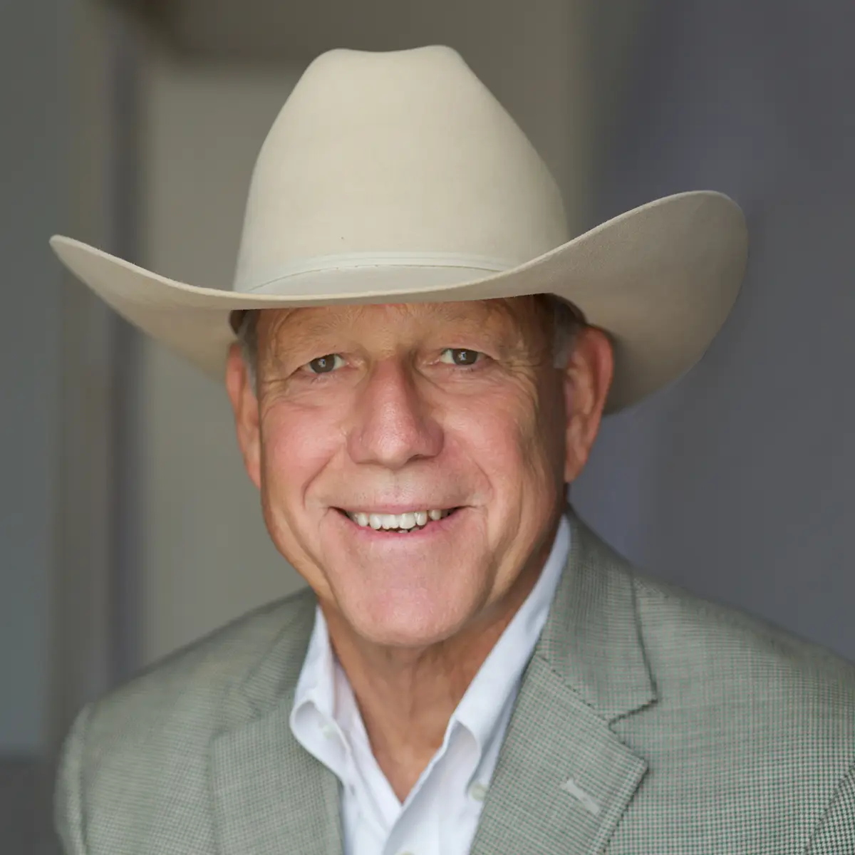 Smiling man wearing a white cowboy hat and light gray blazer, facing the camera.