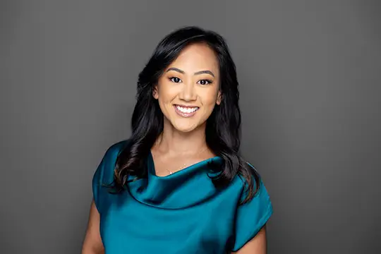Portrait of a Smiling Woman with Dark Hair Wearing a Teal Blouse Against a Gray Backdrop