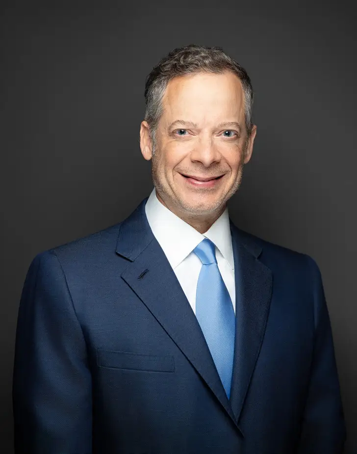 Smiling Man in a Navy Suit and Light Blue Tie Against a Dark Gray Background Corporate Headshot