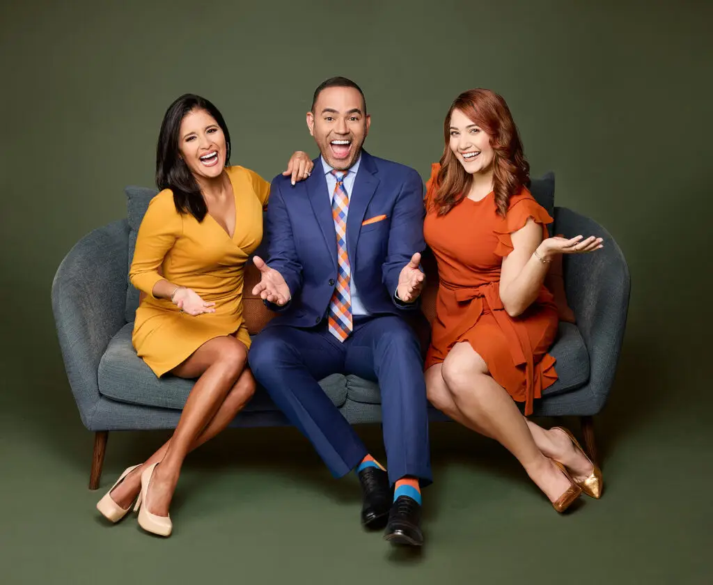 Three Friends Sit on a Gray Sofa Smiling and Posing for the Camera Against a Green Backdrop