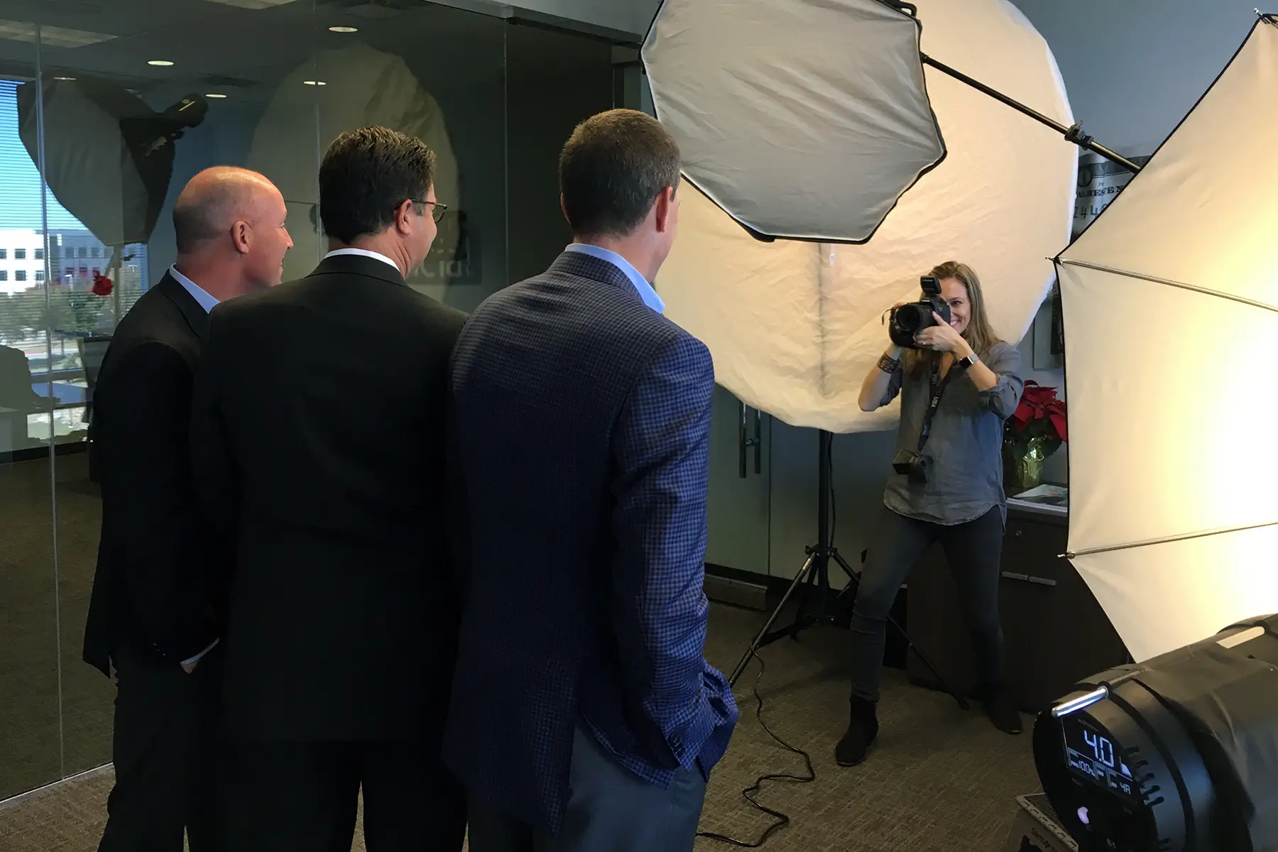 Photographer with a Camera Aiming at Three Men in Suits in a Studio Setup with Large Softbox Lights Nearby Ready to Shoot
