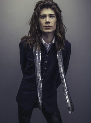 We Will Rock You Male model with long brown hair wearing a sparkle scarf posing in McKinney, TX.