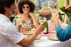 girl in sunglasses and curly brown hair and man drinking champagne outside at table.